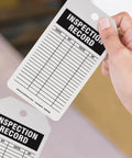 Flat Out Dependable Inspection And Status Record Tags By The Roll Including A Portable Octagon Dispenser And Perforated Center Hole For Easy Workshop Mounting No Sweat Just Quick Peel And Track Daily Grind, writable inspection record tag in hand.