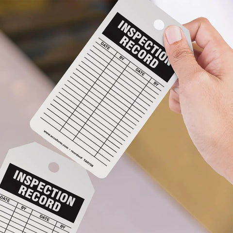 Flat Out Dependable Inspection And Status Record Tags By The Roll Including A Portable Octagon Dispenser And Perforated Center Hole For Easy Workshop Mounting No Sweat Just Quick Peel And Track Daily Grind, writable inspection record tag in hand.