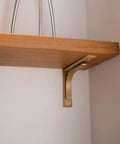 Heavy Duty Shelf Brackets Wall Mount Kickass Brass Metal Supports installed under a wooden shelf holding it securely.