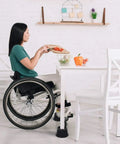 Woman in wheelchair using table with Premium 3 Inch Bed Risers With Steel Reinforced Caster Wheel Holder Top 4 Pack Lifts Up To 2640 Pounds