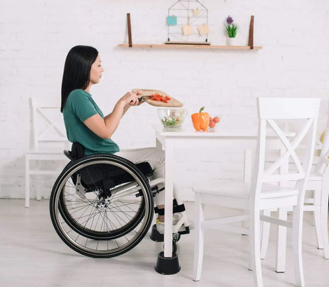 Woman in wheelchair using table with Premium 3 Inch Bed Risers With Steel Reinforced Caster Wheel Holder Top 4 Pack Lifts Up To 2640 Pounds