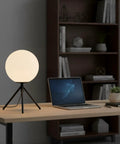 Modern Black Globe Table Lamp With Opal Glass Ball On A Metal Tripod Base Mid Century Inspired Bedside Lamp on desk near laptop