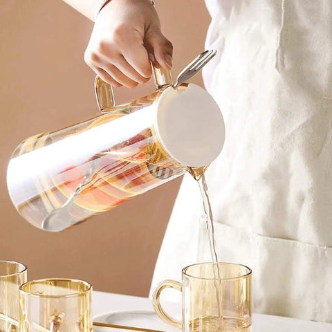 A Game Changer High Borosilicate Glass Pitcher With Secure Tight Lid And Long Mixing Spoon One Point Six Liter Heat Resistant Beverage Carafe pouring tea into a clear glass.