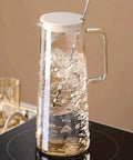 A Game Changer High Borosilicate Glass Pitcher With Secure Tight Lid And Long Mixing Spoon One Point Six Liter Heat Resistant Beverage Carafe Pouring Iced Coffee Tea Juice Milk, filled with water on a stovetop.