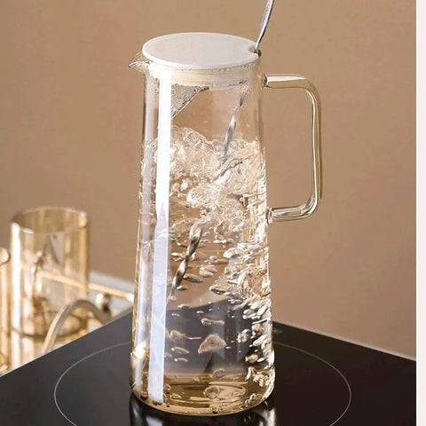 A Game Changer High Borosilicate Glass Pitcher With Secure Tight Lid And Long Mixing Spoon One Point Six Liter Heat Resistant Beverage Carafe Pouring Iced Coffee Tea Juice Milk, filled with water on a stovetop.