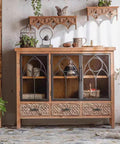 Elegant rustic cabinet with glass doors and intricate carvings, styled with decorative items in a vintage-inspired room.