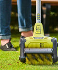 Cordless 18 Volt Patio Surface Cleaner With Telescoping Handle, close-up on scrubbing brush in use on green lawn surface.