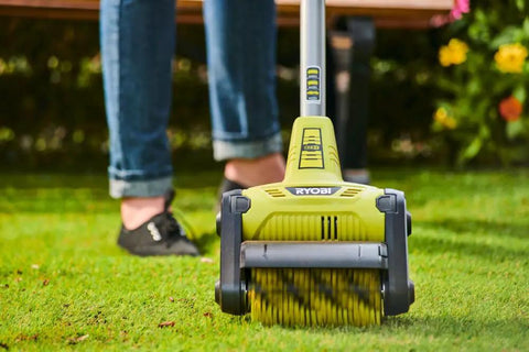 Cordless 18 Volt Patio Surface Cleaner With Telescoping Handle, close-up on scrubbing brush in use on green lawn surface.