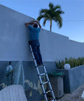 Person using Telescopic Ladder 15.5 Ft Heavy Duty Aluminum Alloy Multi Purpose Collapsible Steps For Home RV Use Safe Slow Down Design Lightweight Portable 330 Lbs Capacity against a wall.