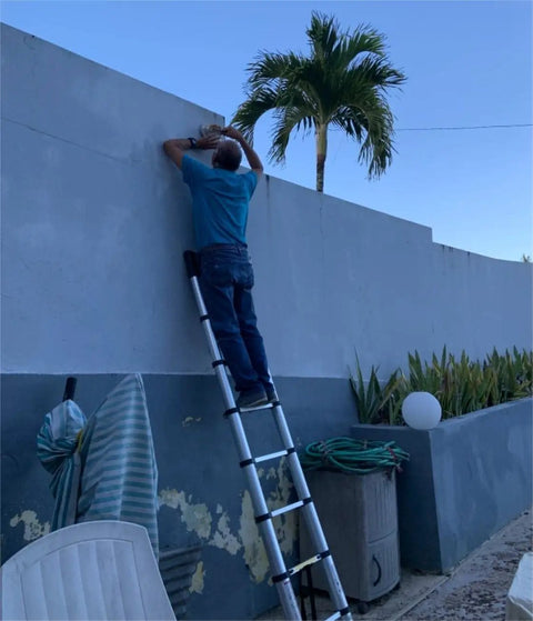Person using Telescopic Ladder 15.5 Ft Heavy Duty Aluminum Alloy Multi Purpose Collapsible Steps For Home RV Use Safe Slow Down Design Lightweight Portable 330 Lbs Capacity against a wall.