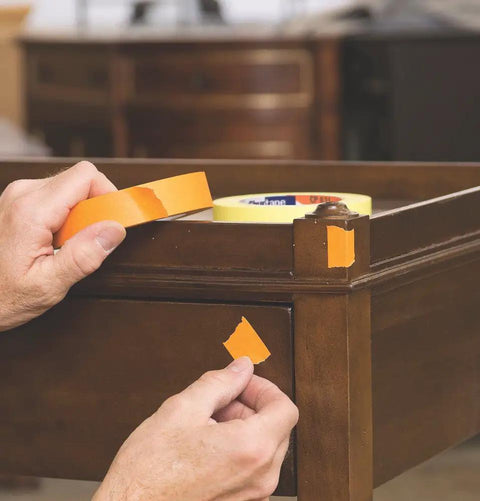 Person applying orange tape to furniture corner, showing flexible crepe backing of CP 631 General Purpose Masking Tape 24mm x 55m White With Medium-High Adhesion
