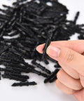 Close-up of a black 1/4-inch barbed irrigation connector held between fingers; many similar fittings visible in background.