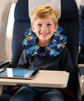 Kids blue truck-print travel neck pillow worn by smiling boy on an airplane with tablet on tray