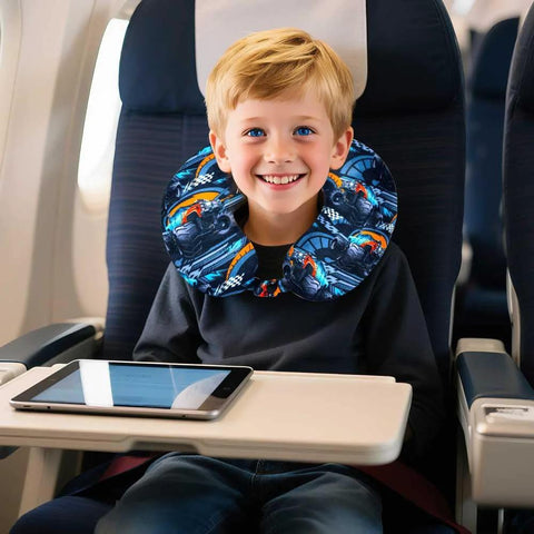 Kids blue truck-print travel neck pillow worn by smiling boy on an airplane with tablet on tray