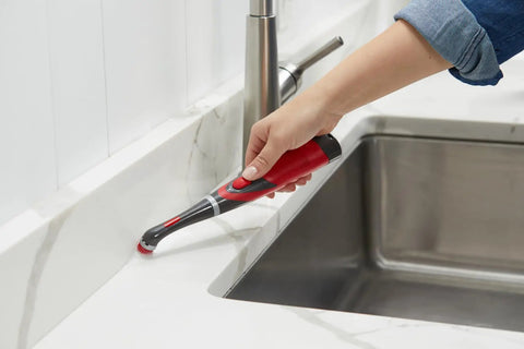 Woman using attachable grout head for cordless power scrubber on countertop grout near kitchen sink