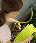 User connecting the Top Tier 5 8 Inch By 75 Foot Garden Hose With Swivel Grip Connectors to a water source in the yard.