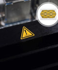 Close-up of a single yellow PVC warning sticker on machinery, part of 24 Pack Yellow PVC Factory Warning Stickers Safety Decals