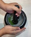 Person using Heavy Duty Granite Mortar And Pestle Set 6 Inch Stone Grinder for fresh herbs on a white surface