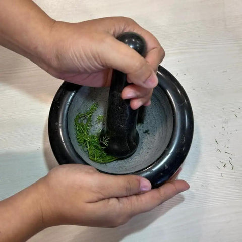 Person using Heavy Duty Granite Mortar And Pestle Set 6 Inch Stone Grinder for fresh herbs on a white surface