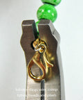 Close-up of Crimping Pliers For Jewelry Making And Beading holding a gold lobster clasp with green beads in background