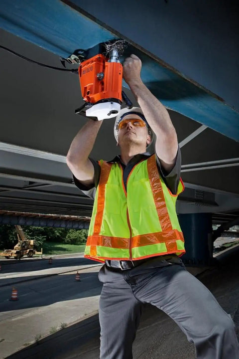 Worker using Heavy Duty Magnetic Drill Sized For One Point Six Two Five Inch Boring on steel beam in safety gear.