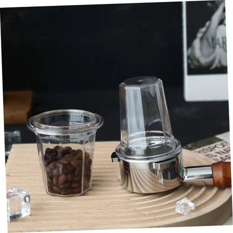 Clear espresso dosing cup for coffee machines, anti scatter powder design, next to a portafilter on a wooden base