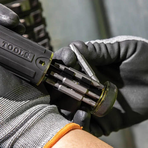 Close-up of gloved hands holding Ratcheting Multi-Bit Screwdriver 15-In-1 With Phillips Slotted Square Torx bits open on-handle storage.