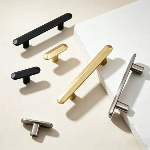 Variety of T-bar cabinet handles including black, gold, and satin nickel finishes on a light surface.