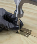 General Tools 806 Jiffy Centering Punch, silver; close-up of center punch pressed into hinge plate on wood with gloved hand