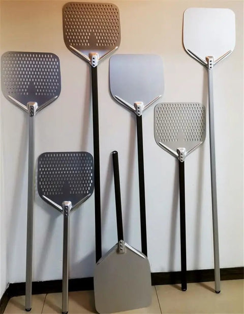 Assortment of Long Handled Aluminum Pizza Peel With Nonstick Perforated Surface, 12 Or 14 Inch, standing upright against wall