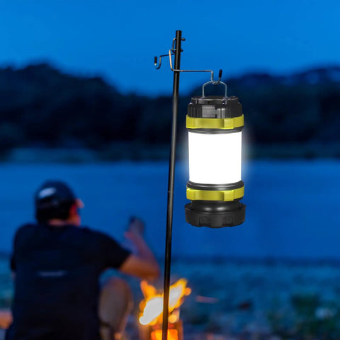 Two Pack LED Camping Lanterns That Are Lit With 1000LM hanging outdoors by a campfire with a person sitting nearby at dusk.