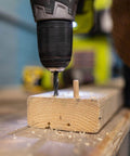 Power drill next to 1/4-Inch Fluted Wood Dowel Pins inserted into wood block, showing chamfered ends for easy insertion.