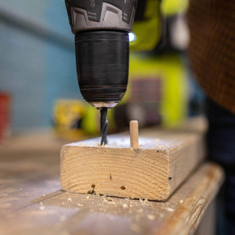 Power drill next to 1/4-Inch Fluted Wood Dowel Pins inserted into wood block, showing chamfered ends for easy insertion.