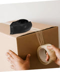 Rock Solid Heavy Duty Tape Dispenser Cutter With Ergonomic Grip And Sharp Steel Blade For 5 Cm Packing Tape in use on a cardboard box.
