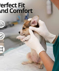 A person wearing white gloves holds a puppy during a medical examination, showcasing Straight Up Reliable Disposable Nitrile Exam Gloves, White Powder Free Build, Rock Solid 3 Mil Coverage For Medical Rounds, Kitchen Prep, Barber Work, Or Heavy Duty Home Cleaning, Box Of 100.