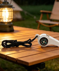 3-In-1 Survival Whistle With Built-In Compass And Thermometer resting on a wooden table near camping lantern