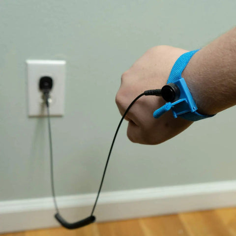 Person wearing Anti Static ESD Wrist Strap Kit with blue wristband and black coil cord, plugged into wall for safe electronics handling