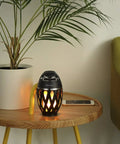 LED Flame Outdoor Table Lamp With Bluetooth Speaker Rechargeable Ambience Lantern With Flickering Warm Light on a round table.