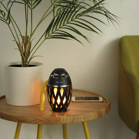 LED Flame Outdoor Table Lamp With Bluetooth Speaker Rechargeable Ambience Lantern With Flickering Warm Light on a round table.