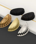 Set of assorted metallic cup pulls on a black and white surface, showing matte black, bronze, gold, and silver finishes for cabinets.
