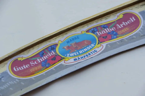 Close-up of branded label on Hand Forged Austrian Scythe Blade With 23.5 Inch Length Dual 50mm And 55mm Sweeps Sharp And Ready To Use