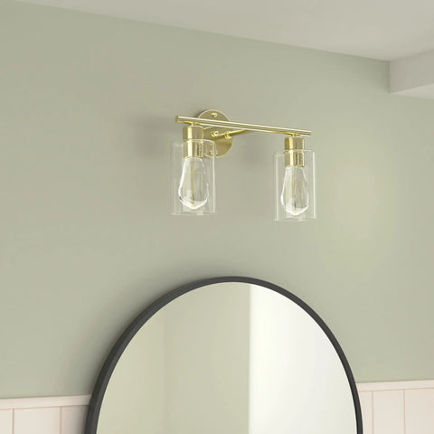 Dope Gold Vanity Light Fixture With Glass Shade Brushed Brass Wall Sconces above round mirror on pastel wall.