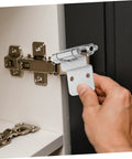 Unomor inset cabinet hinge in silver metal being installed on a cabinet door.