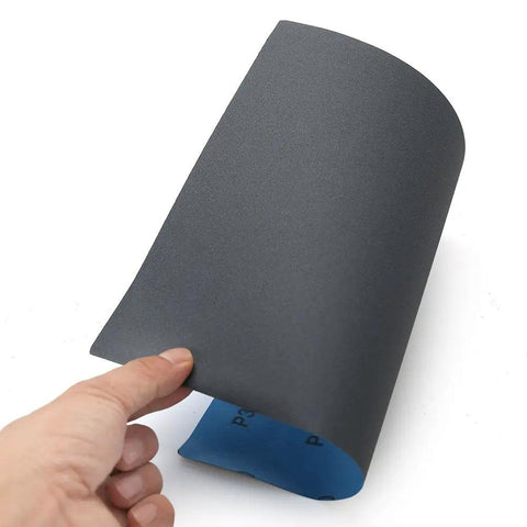 Close-up of a hand holding a 320 Grit Sandpaper Pro Grade 9 By 11 Inches Pack Of 30 Sheets Silicon Carbide for dry and wet sanding.