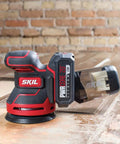 PWRCore 20 Brushless 20V 5-Inch Random Orbital Sander with 2.0Ah Battery and PWRJump Charger on wood surface
