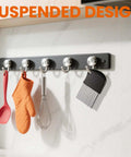 Black wall-mounted kitchen rail with metal hooks holding spatula, oven mitt, whisk, and brush