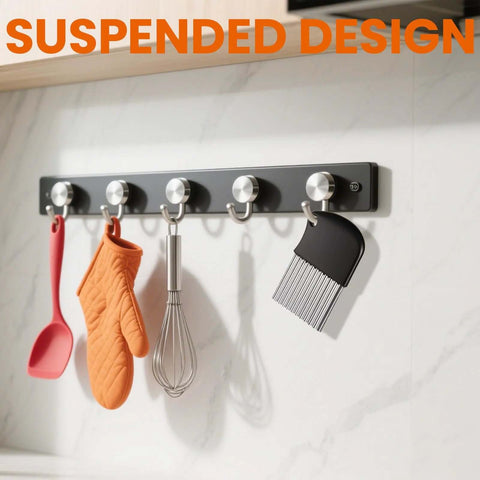 Black wall-mounted kitchen rail with metal hooks holding spatula, oven mitt, whisk, and brush
