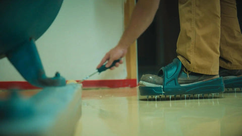 Person applying epoxy floor wearing Spiked Shoes For Resinous Epoxy Floor Coatings With Replaceable Spikes Slip On Quick Fit