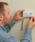 Person installing No Drill Wall Mount For Carbon Monoxide Alarms Battery Back Cover Included Upgrade With Lanyard Portable Design And Quick Release Bracket So Easy To Install No Drilling Alarms Not Included on wall.