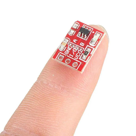 Close-up of a TTP223 capacitive touch switch module on a finger for Arduino projects, 15x11mm size, red PCB, part of Twenty Piece Capacitive Touch Switch Modules TTP223 2.5 To 5.5V Self Lock Or No Lock For Arduino Maker Friendly Touch Button Sensor 15 By 11 Millimeters Plug And Play DIY Projects.